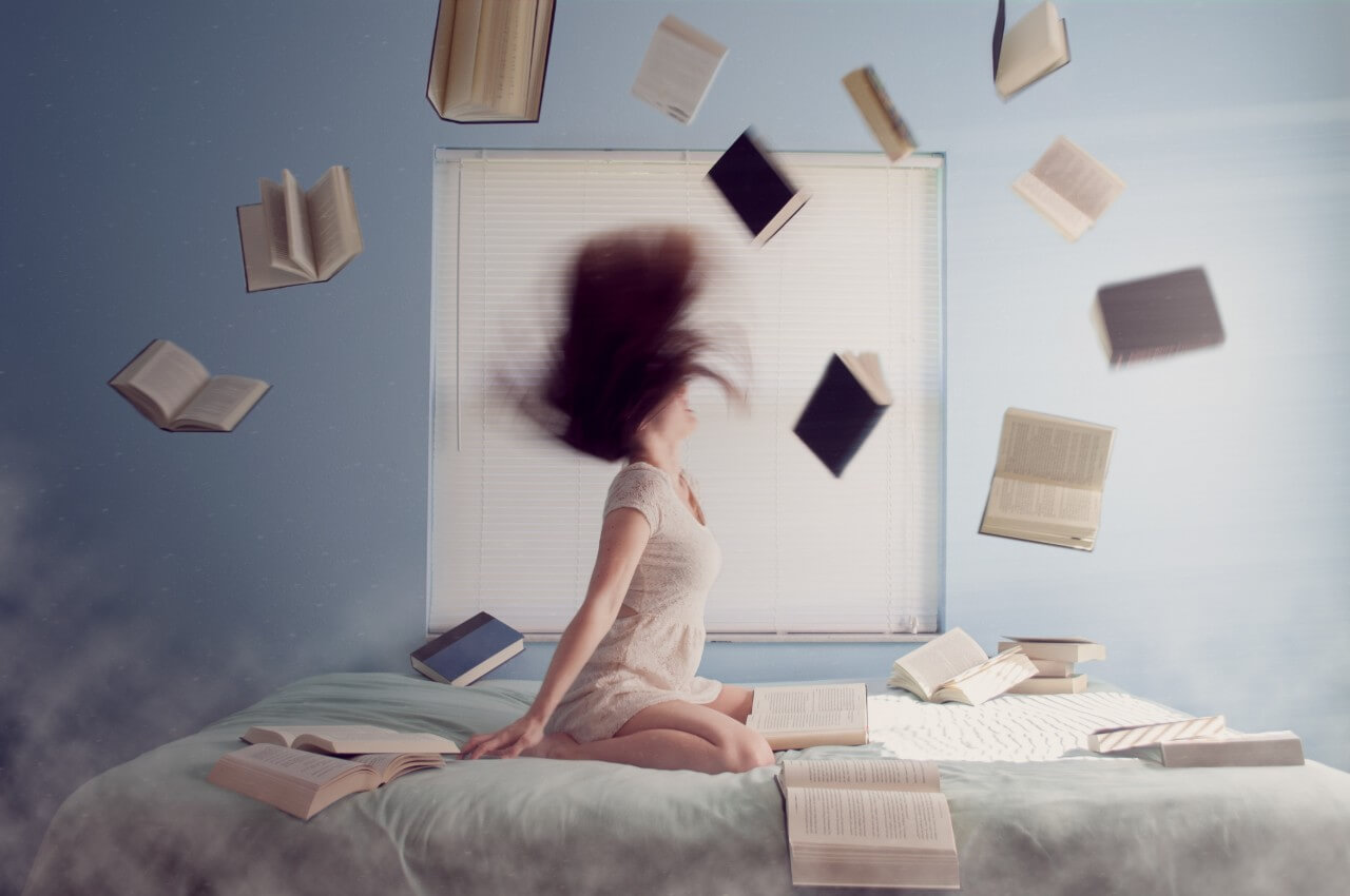 A woman on a bed throwing lots of books into the air