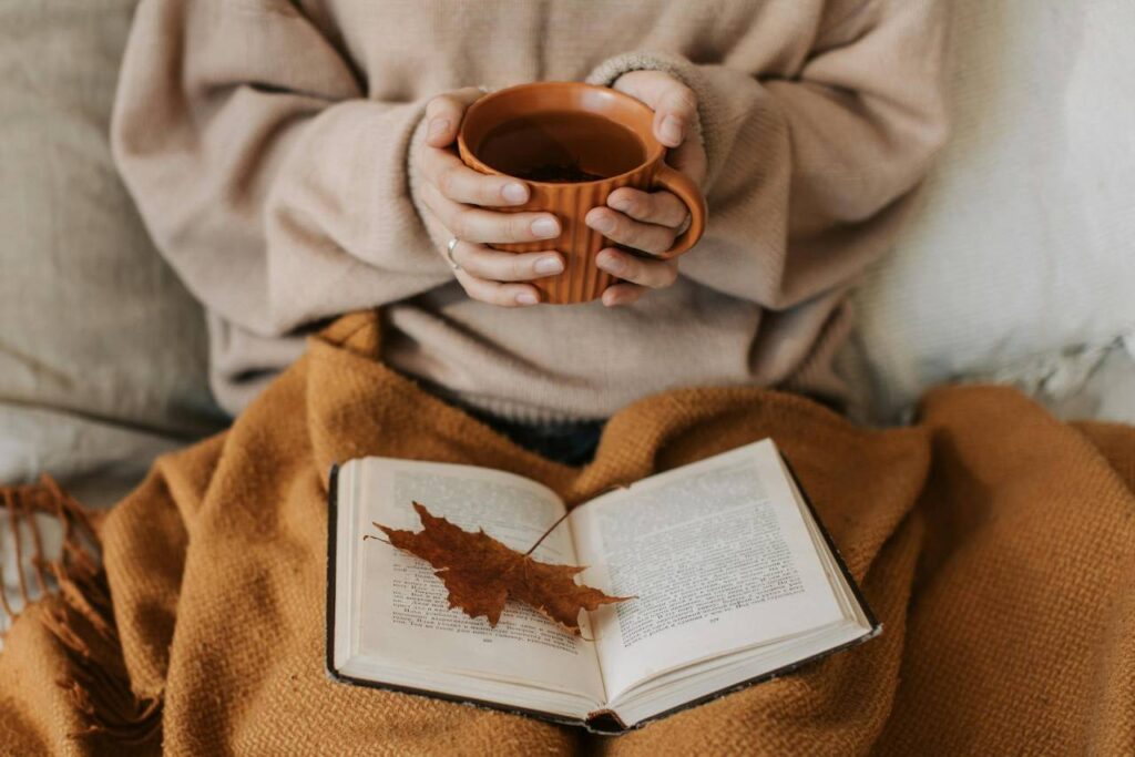 woman holding a cup of coffee with an open book and a maple leaf in the book